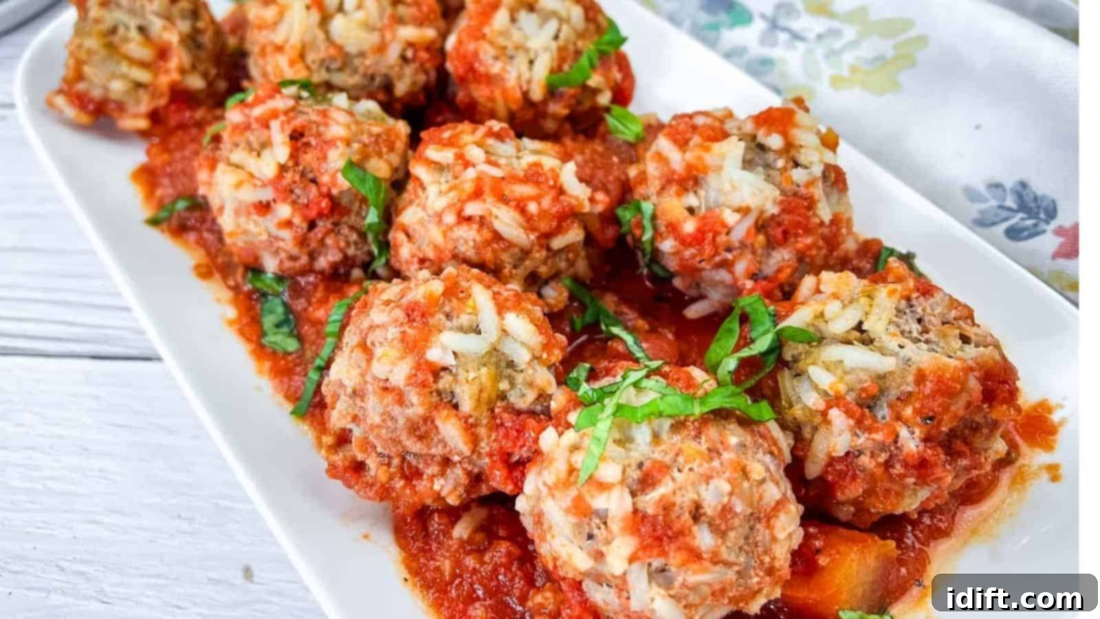 17 Ground Beef Recipes Too Good For Cookbooks 18 A rectangular plate of Slow Cooker Porcupine Meatballs generously covered in a savory tomato sauce and garnished with fresh basil.