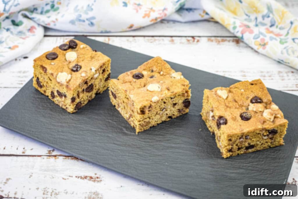 Three pieces of pumpkin blondies are arranged side by side on a black rectangular slate, ready to be enjoyed.