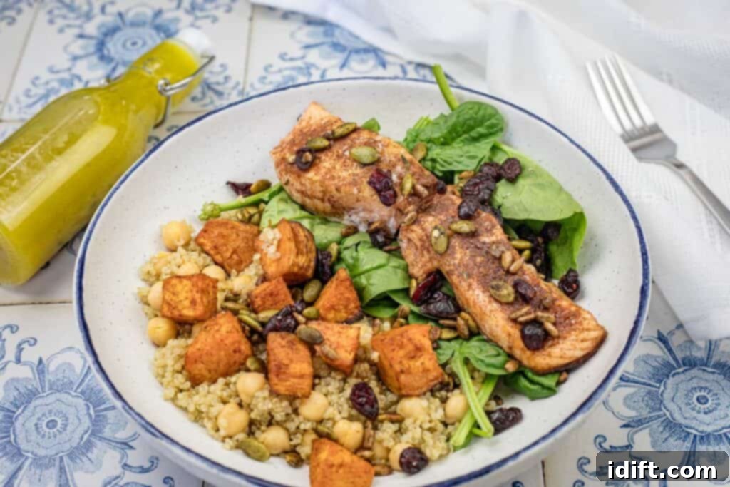 Golden Autumn Salmon Bowl 15 A beautifully assembled salmon bowl on a plate, featuring flaky roasted salmon, colorful sweet potatoes, fluffy quinoa, and fresh spinach, all generously drizzled with citrus dressing and topped with a vibrant crunch mix, ready to be enjoyed.