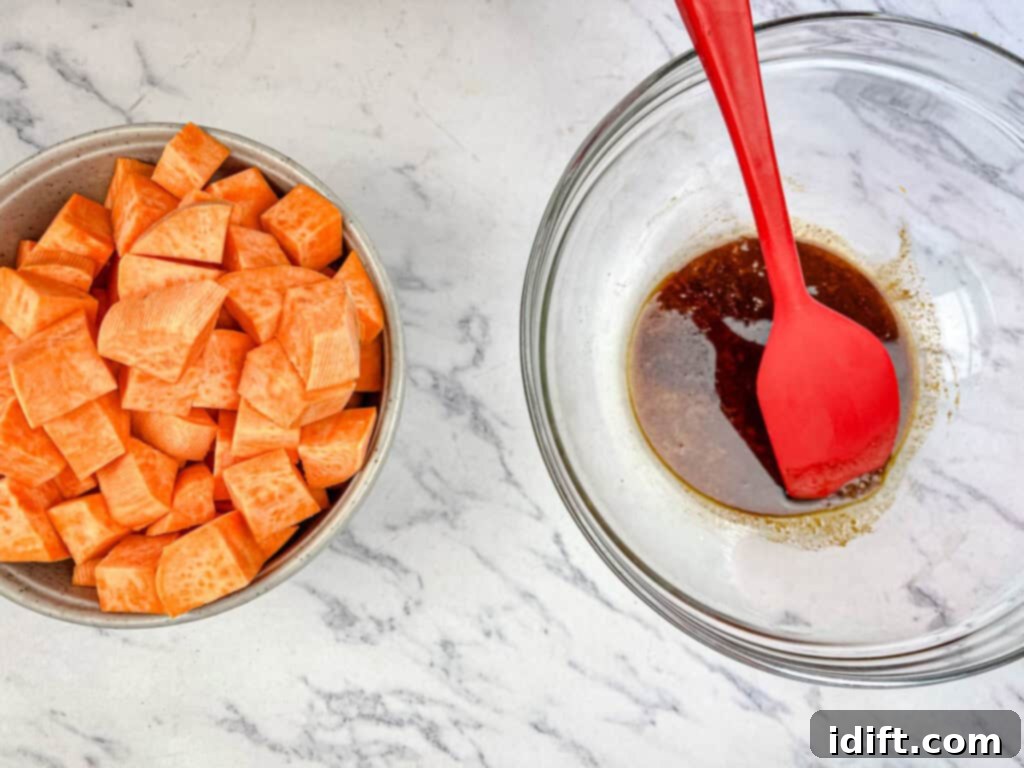 Golden Autumn Salmon Bowl 8 A large bowl containing cubed sweet potatoes, generously tossed with olive oil, chili powder, fresh orange zest, and a sprinkle of salt, ensuring an even coating for roasting.