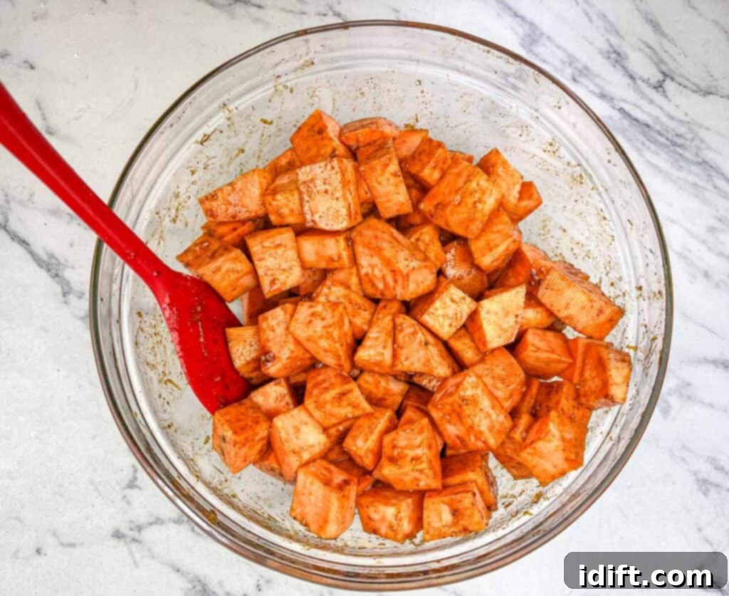 Golden Autumn Salmon Bowl 9 Seasoned sweet potato cubes spread out in a single, even layer on a baking sheet, ready for roasting to achieve tender, caramelized perfection.