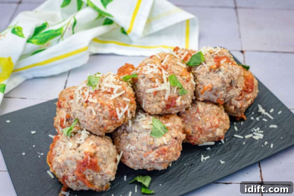 A stack of perfectly cooked and seasoned giant meatballs, garnished with fresh herbs and grated cheese, presented on a stylish black rectangular slate plate, with a lemon-patterned cloth in the soft focus background.