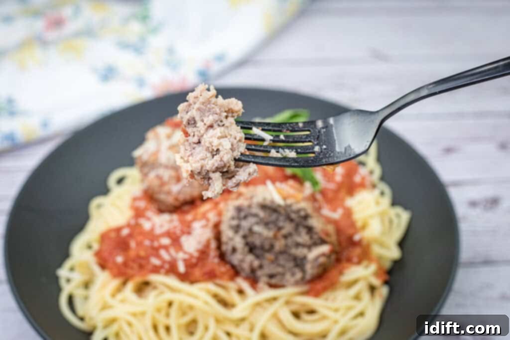 A fork lifts a single, succulent giant meatball above a beautifully plated dish of spaghetti, generously coated in tomato sauce and topped with shredded cheese, highlighting the delicious texture and size of the meatball.