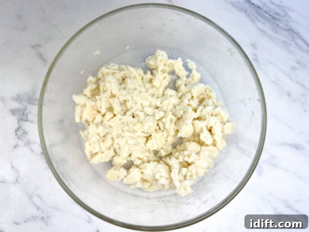 Hands mashing milk-soaked bread slices with a fork in a bowl, transforming them into a smooth, consistent panade.