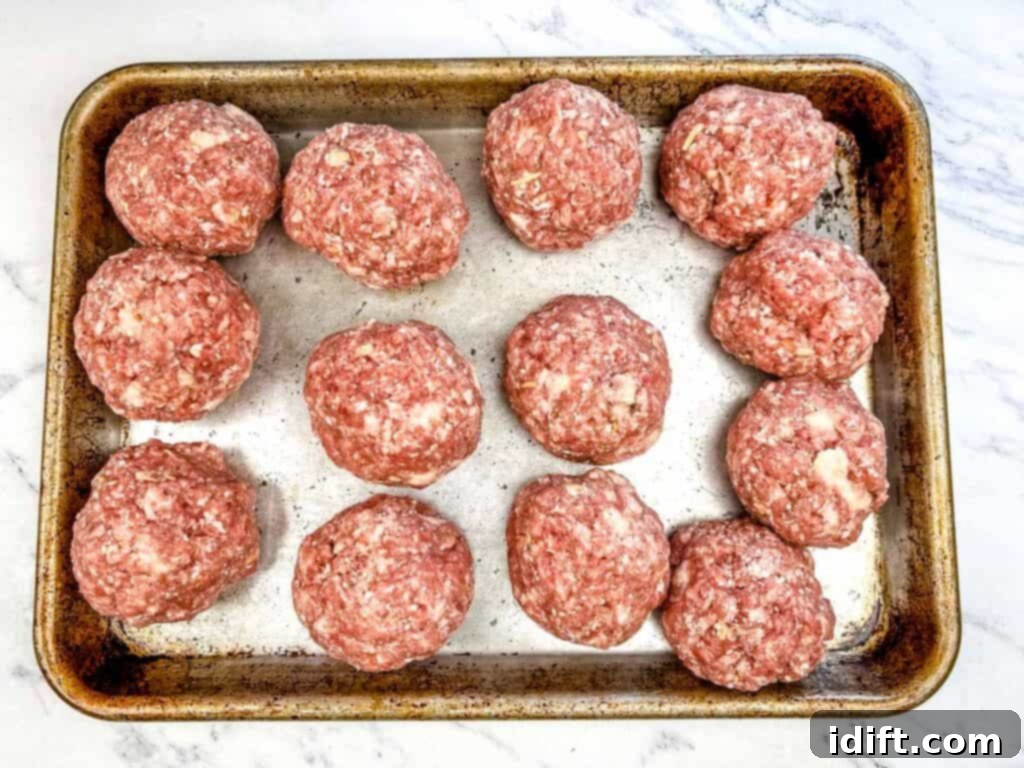 Close-up of uncooked meat mixture being formed into uniform balls and placed on a parchment-lined baking sheet, ready for the oven.