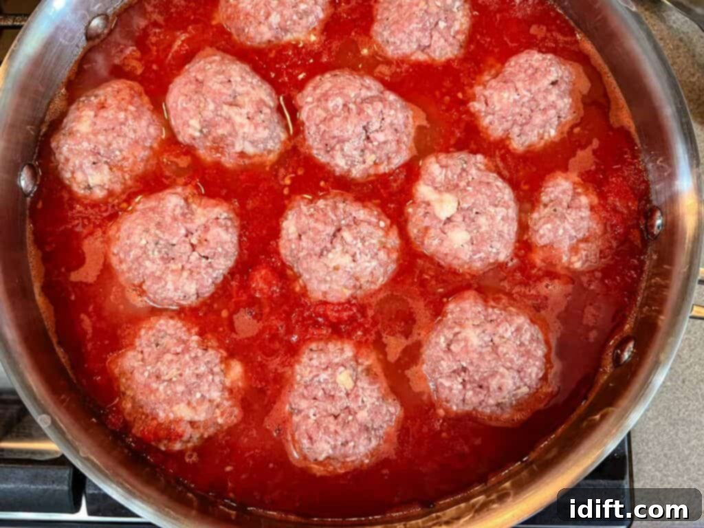 A pan filled with beautifully browned giant meatballs simmering in a rich, bubbling tomato-based sauce on a stovetop, ready to be served.
