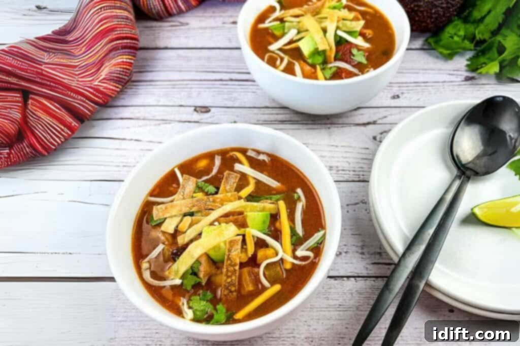 Southwestern Turkey Tortilla Soup 3 Two bowls of Turkey Tortilla Soup with a plate and spoons beside on a wooden table.