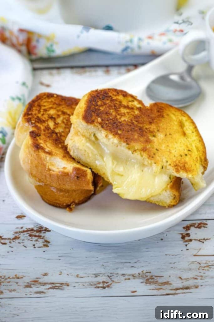 A freshly made Garlic Bread Grilled Cheese sandwich, cut in half and placed on a white plate, showcasing its golden crust and melted cheese.