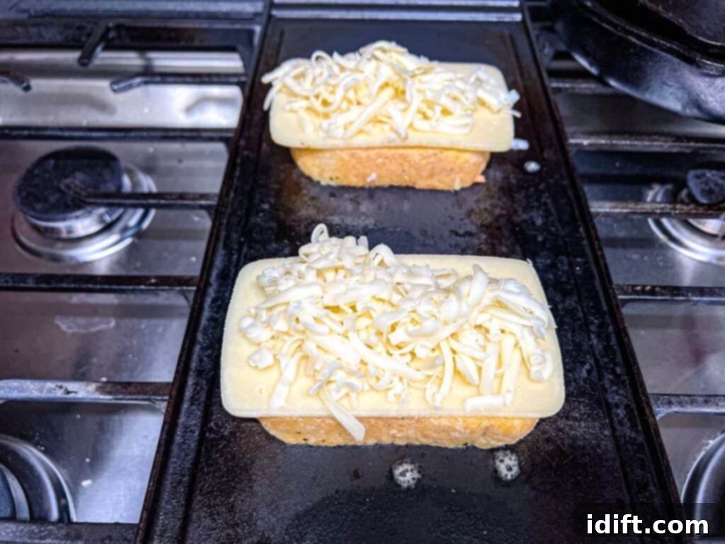 Close-up of shredded mozzarella being sprinkled evenly over sliced cheese on a piece of garlic bread.