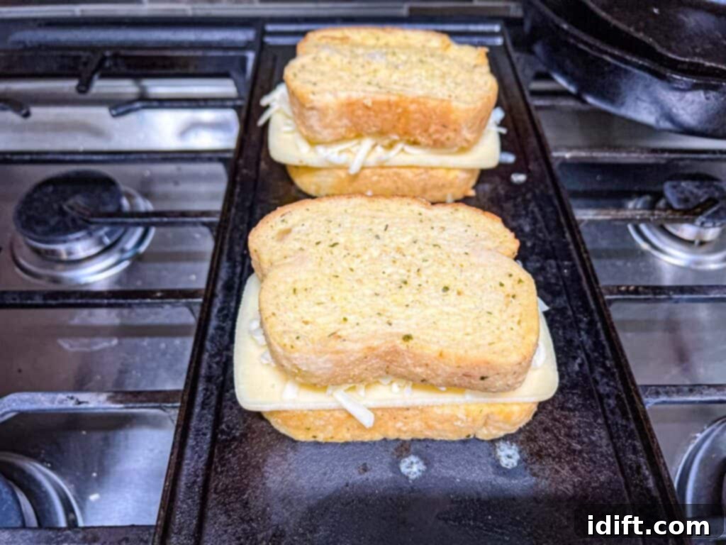 A second slice of garlic bread, buttered side up, being placed on top of a cheese-filled sandwich.