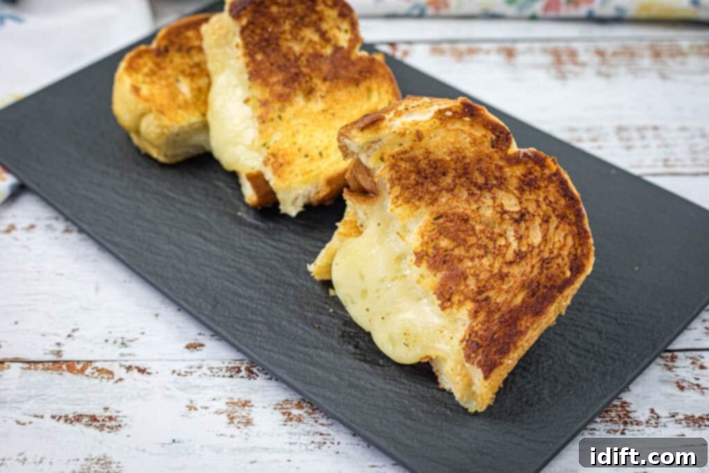Finished Garlic Bread Grilled Cheese slices, perfectly golden and cheesy, displayed on a dark slate plate, ready to be enjoyed.