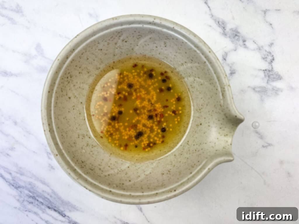 A small bowl showing the mixed marinade ingredients: vegetable oil, vinegar, garlic, sugar, mustard seeds, and red pepper flakes.