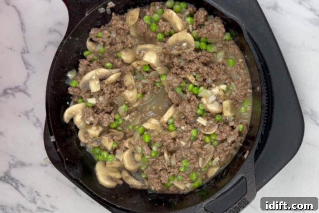 Frozen peas being folded into the thickened beef stroganoff sauce.