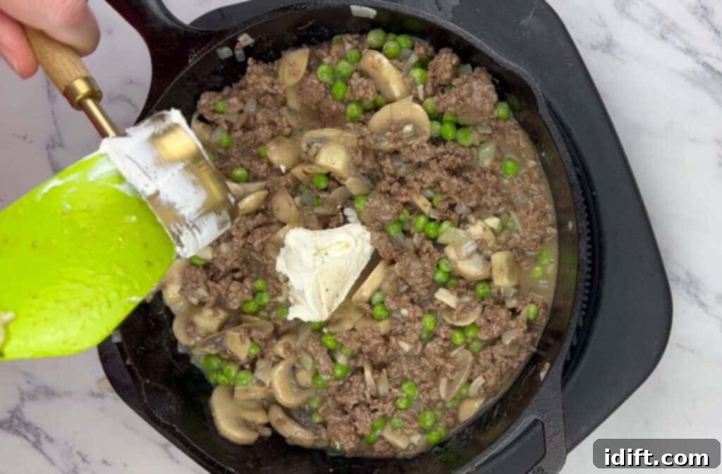 Sour cream being stirred into the beef stroganoff mixture in the skillet.