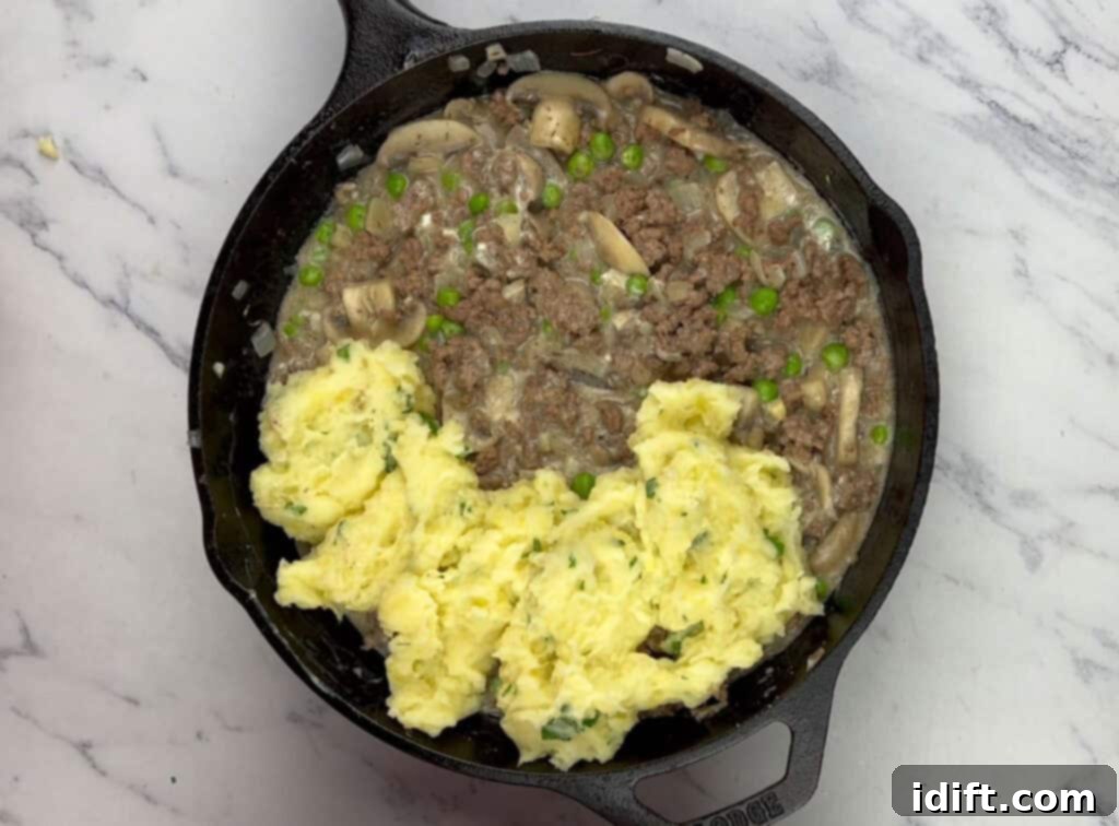 Mashed potatoes being spread evenly over the beef stroganoff filling in the skillet.