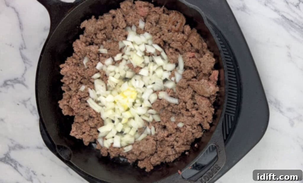 Diced onions, chopped garlic, and dried thyme being added to the skillet with ground beef.