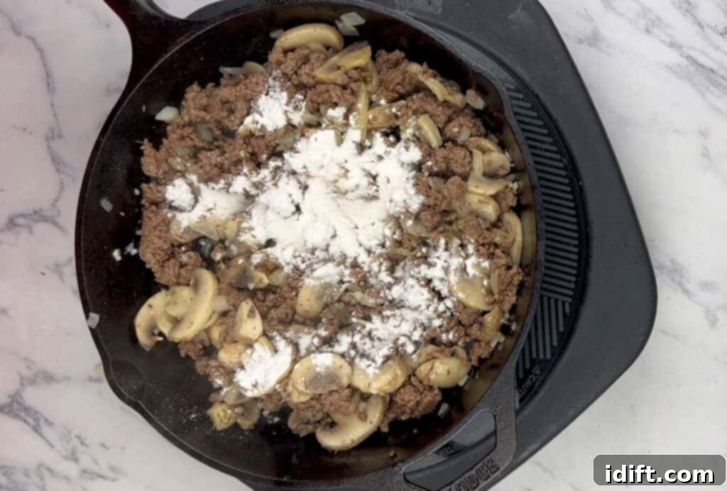 Flour being sprinkled over the beef and mushroom mixture, followed by water to create a thick sauce.