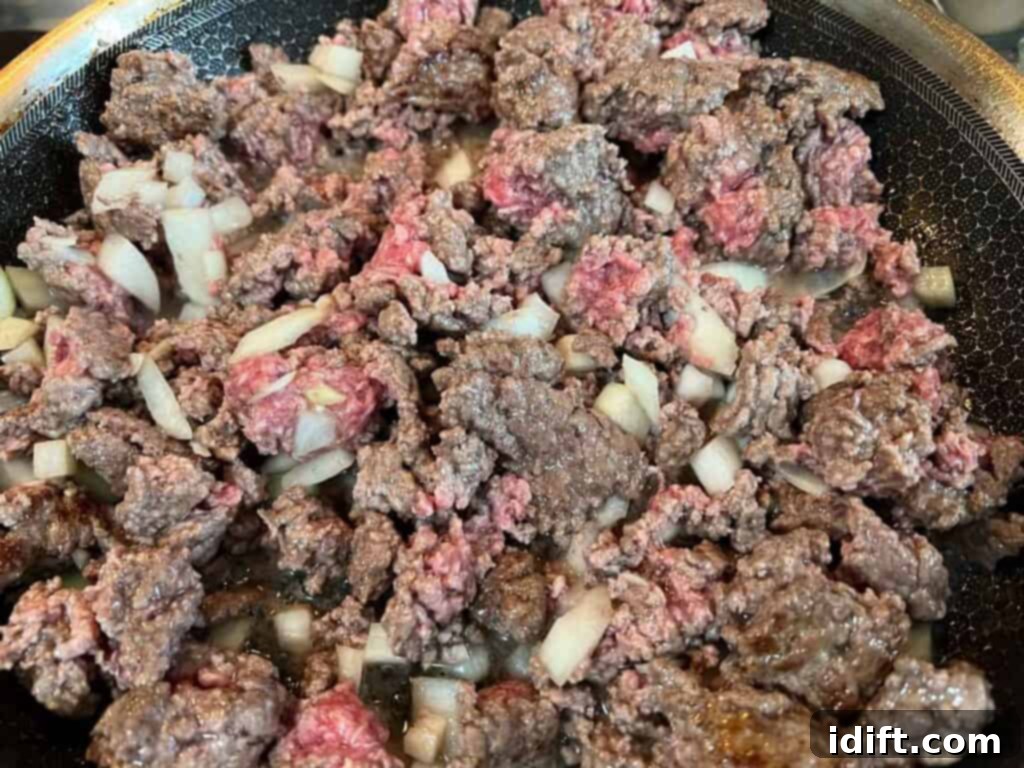 Adding diced onion and garlic to browned ground beef in a skillet.