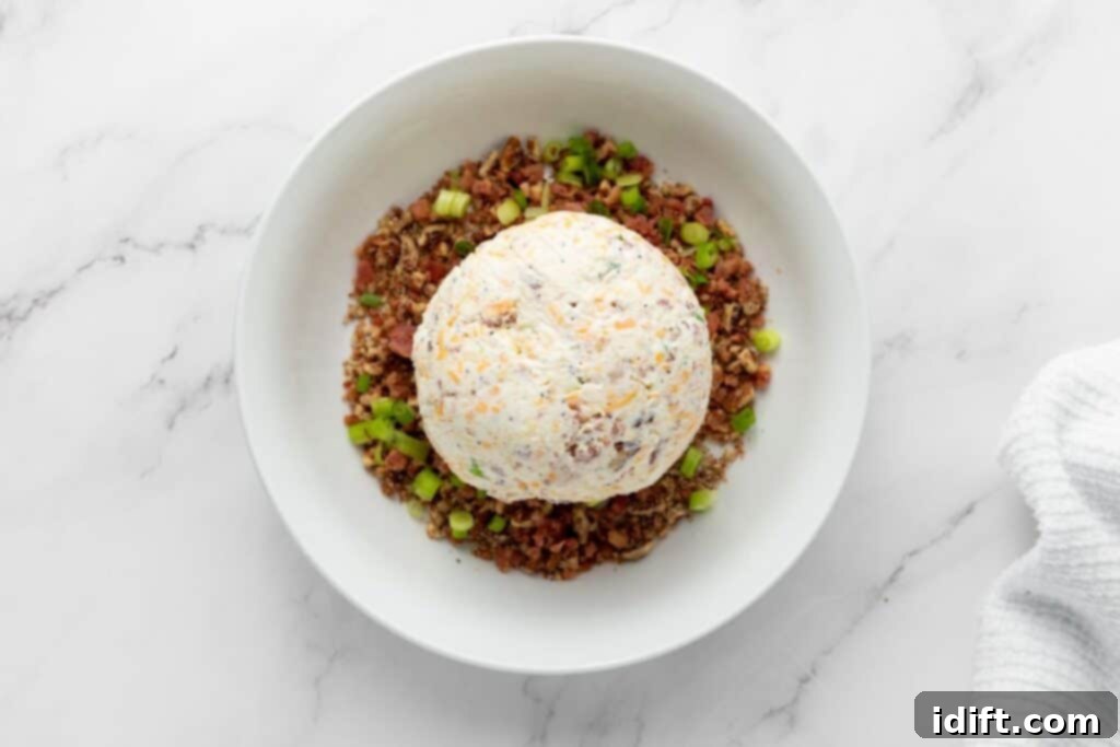 Roll the chilled cheeseball in the prepared coating mixture.