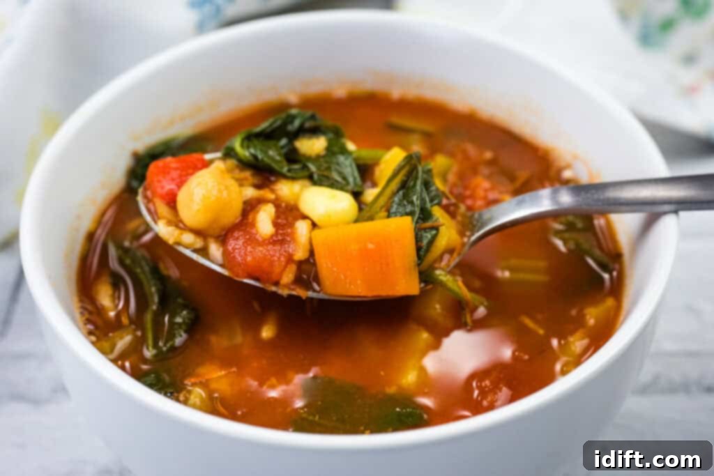 A spoonful of Copycat Panera Bread’s 10 Vegetable Soup being lifted from a bowl, highlighting its chunky texture and colorful vegetables.