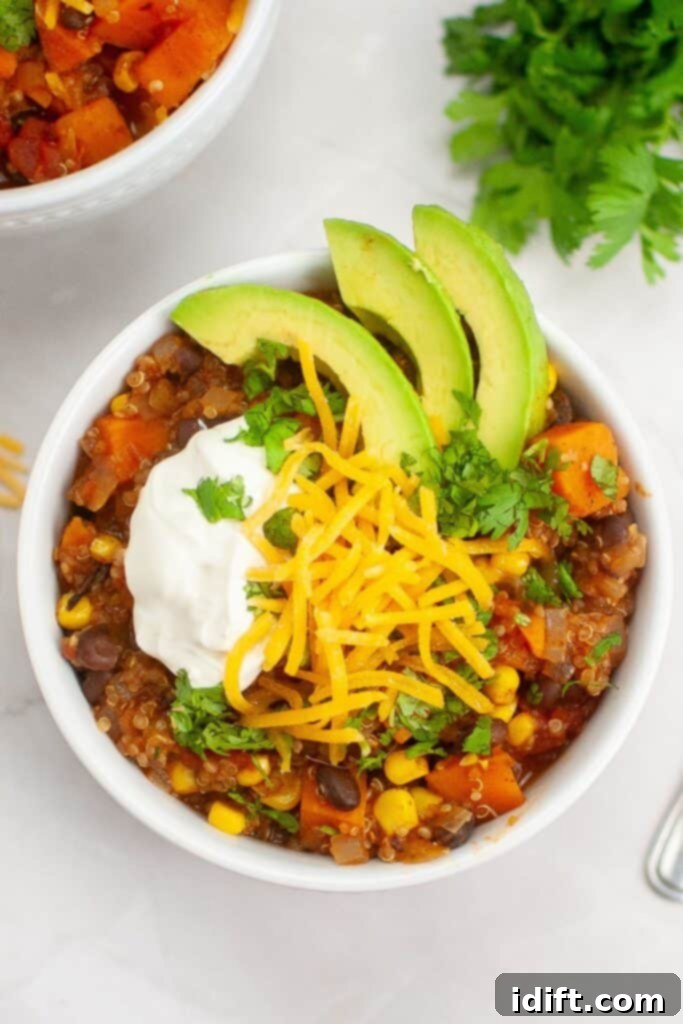 Top-down shot of a white bowl of Sweet Potato Chili with Quinoa, garnished with fresh cilantro and a dollop of sour cream.
