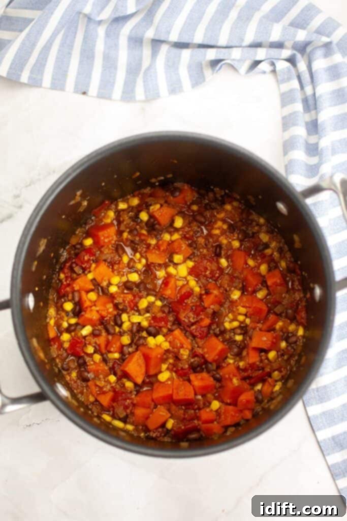 Corn niblets are being stirred into the simmering Sweet Potato Chili with Quinoa in a pot.