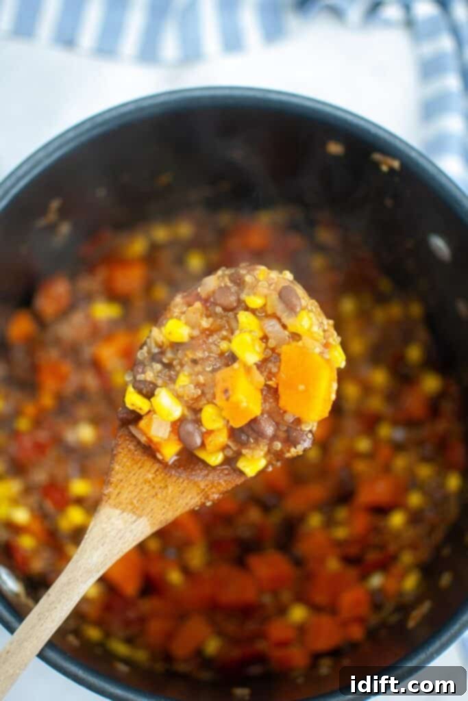A ladle scooping hearty Sweet Potato Chili with Quinoa into a white serving bowl.