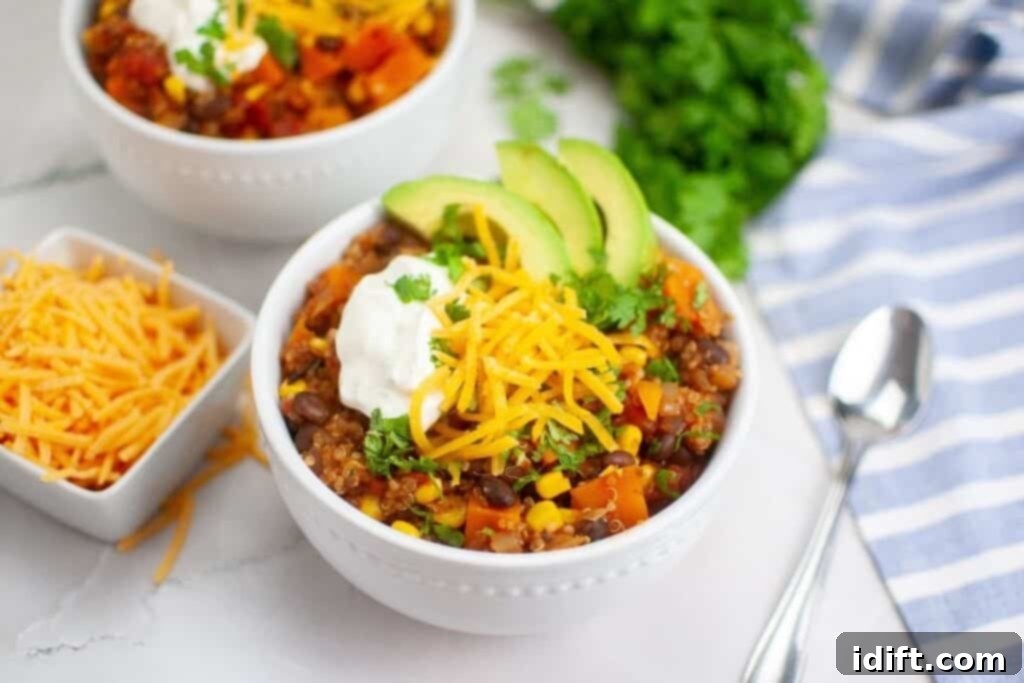 Two bowls of Sweet Potato Chili with Quinoa generously topped with grated cheese, fresh cilantro, a swirl of crema, and creamy avocado slices.