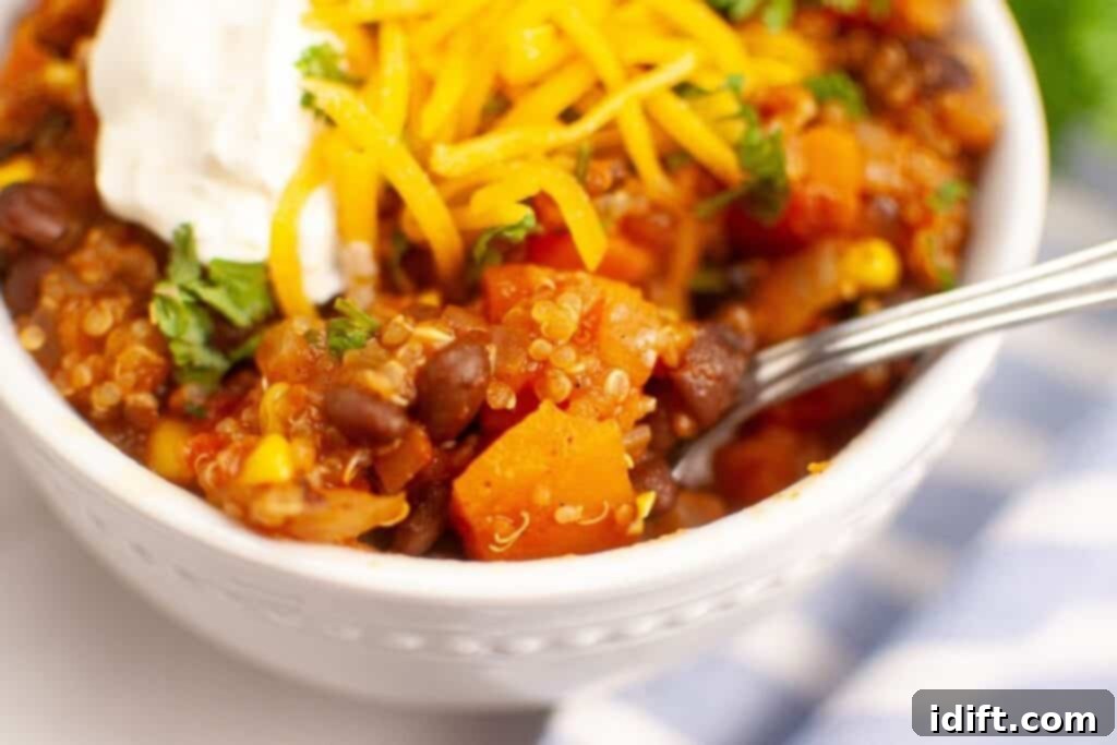 A spoonful of hearty Sweet Potato Chili with Quinoa being lifted from a white bowl, showcasing the rich texture and ingredients.
