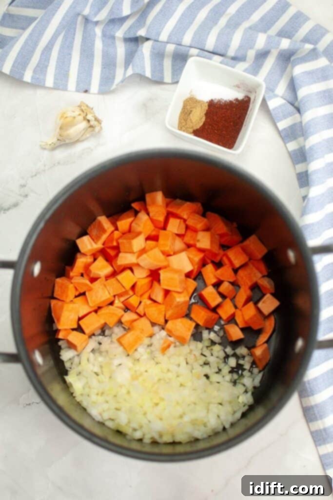 Diced sweet potato and chopped yellow onion are being added to a large pot with heated olive oil, ready for sautéing.