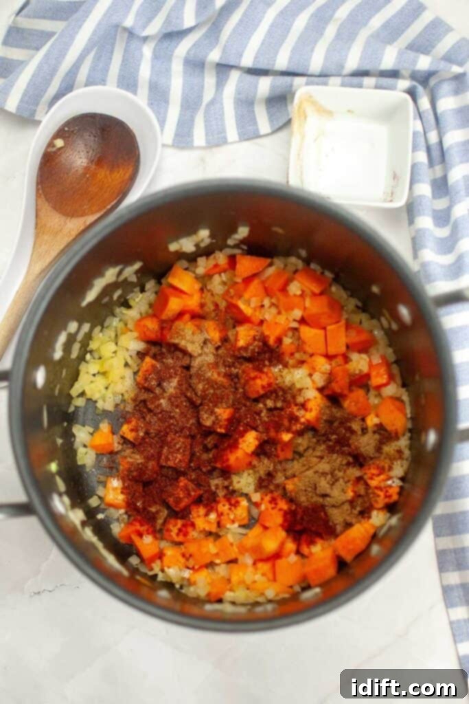 Chopped garlic, chili powder, chipotle powder, cumin, and salt are being stirred into the pot with sautéed vegetables.