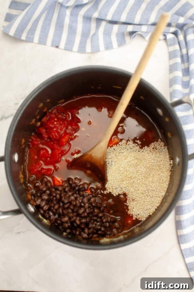 Vegetable broth, fire-roasted tomatoes, black beans, and quinoa are being added to the pot with the spiced vegetables.
