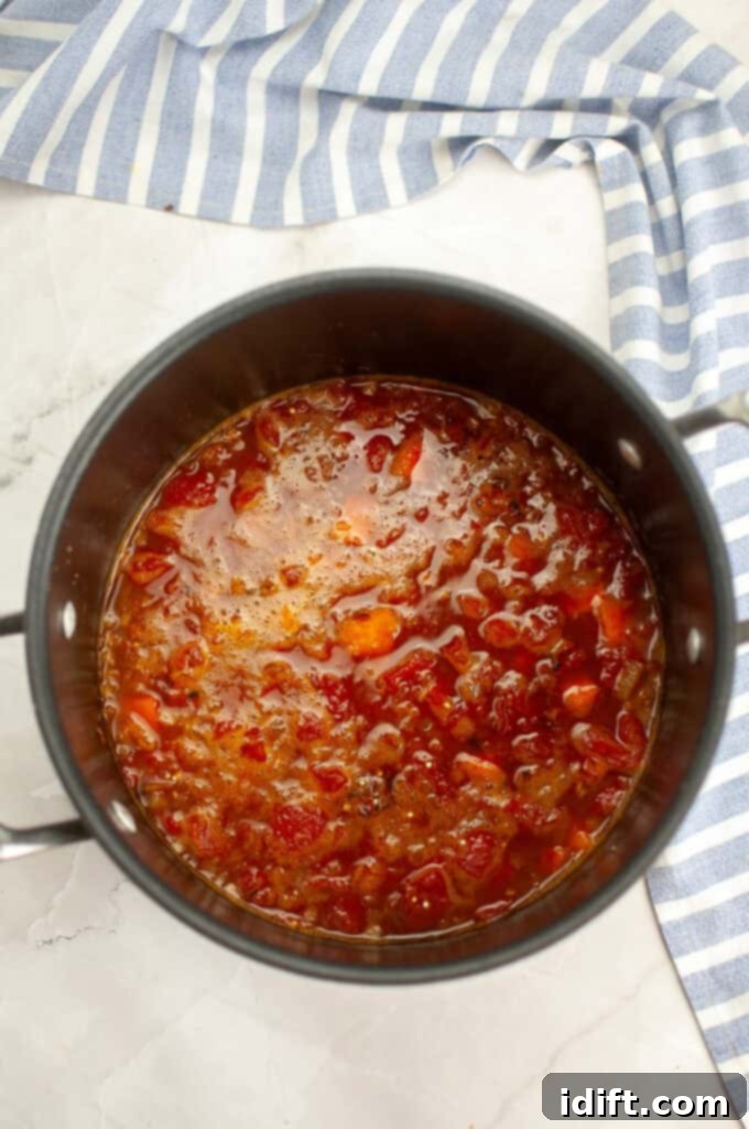 The Sweet Potato Chili with Quinoa simmering gently in a large pot, with a visible lid, indicating the cooking process.