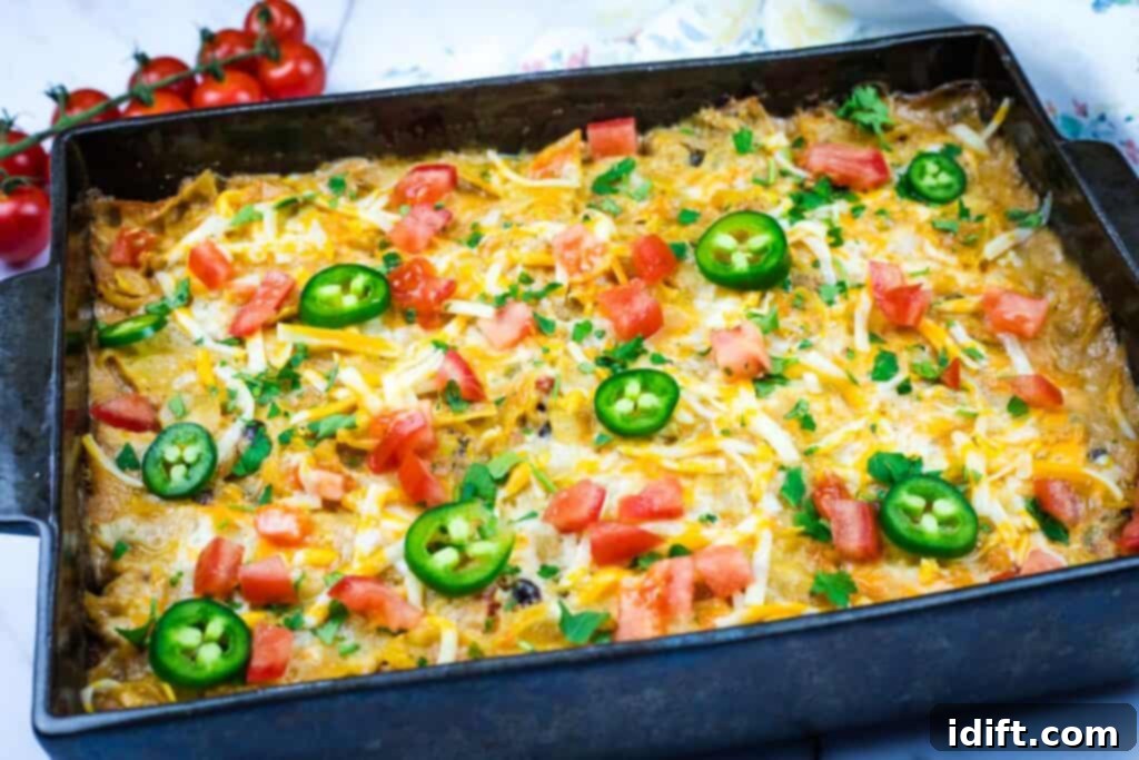A Cheesy Mexican Casserole topped with sliced jalapeños, diced tomatoes, cheese, and herbs in a rectangular pan.