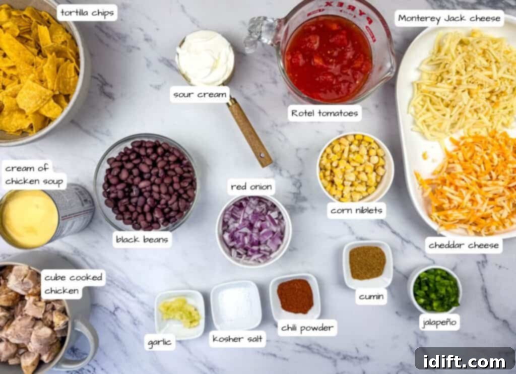 Ingredients for Cheesy Mexican Casserole laid out on a marble surface, including tortilla chips, sour cream, Rotel tomatoes, cheeses, chicken, black beans, red onion, corn, garlic, seasonings, and jalapeño.