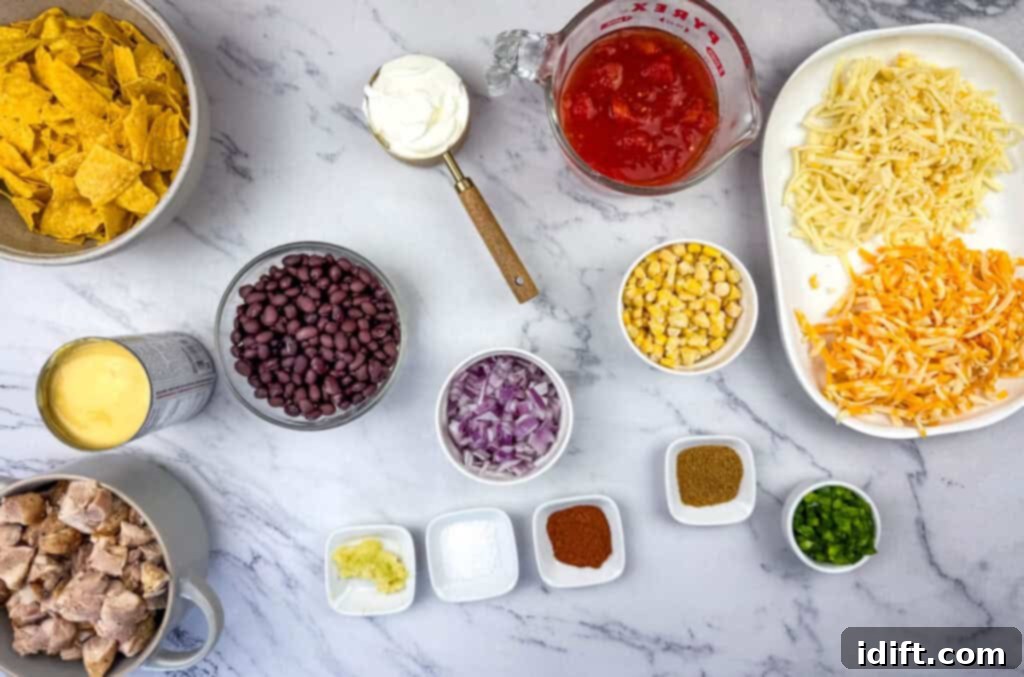 Ingredients for Cheesy Mexican Casserole, including tortilla chips, sour cream, canned beans, corn, cheese, diced tomatoes, chicken pieces, chopped onions, and seasonings like cumin and chili powder on a counter.