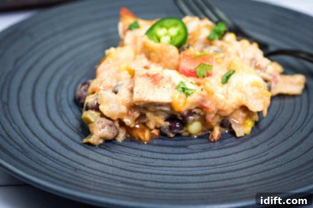 A serving of Cheesy Mexican casserole with melted cheese, vegetables, and a slice of jalapeño on a dark plate, with a fork in the background.