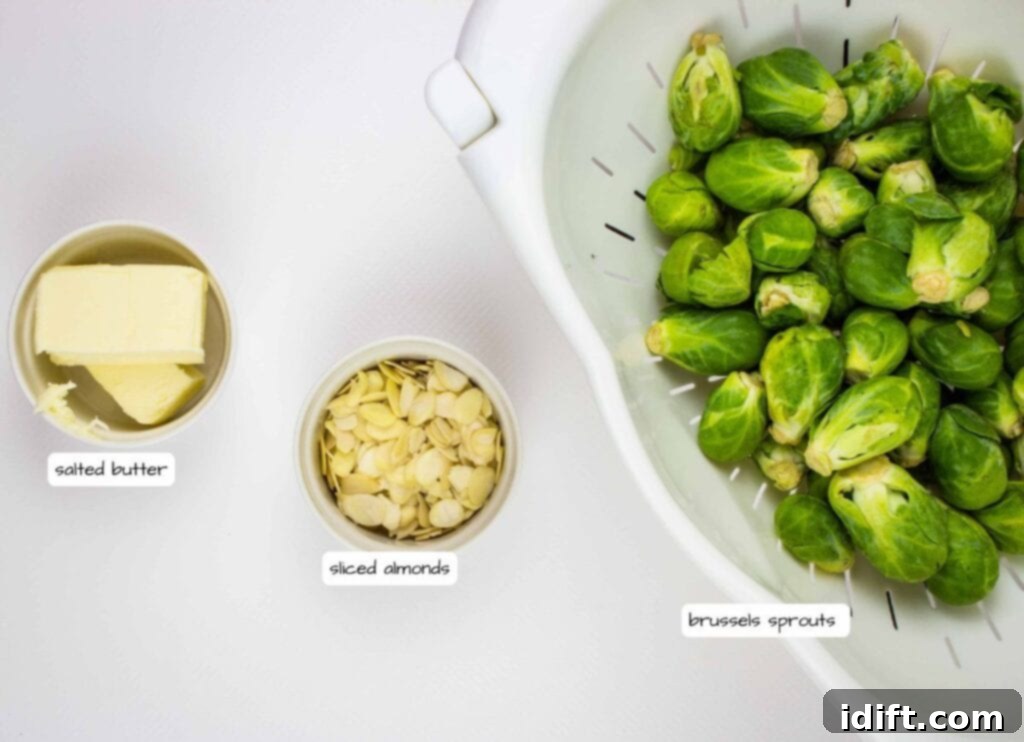 A bowl of salted butter, a bowl of sliced almonds, and a colander filled with brussels sprouts are arranged on a white surface.