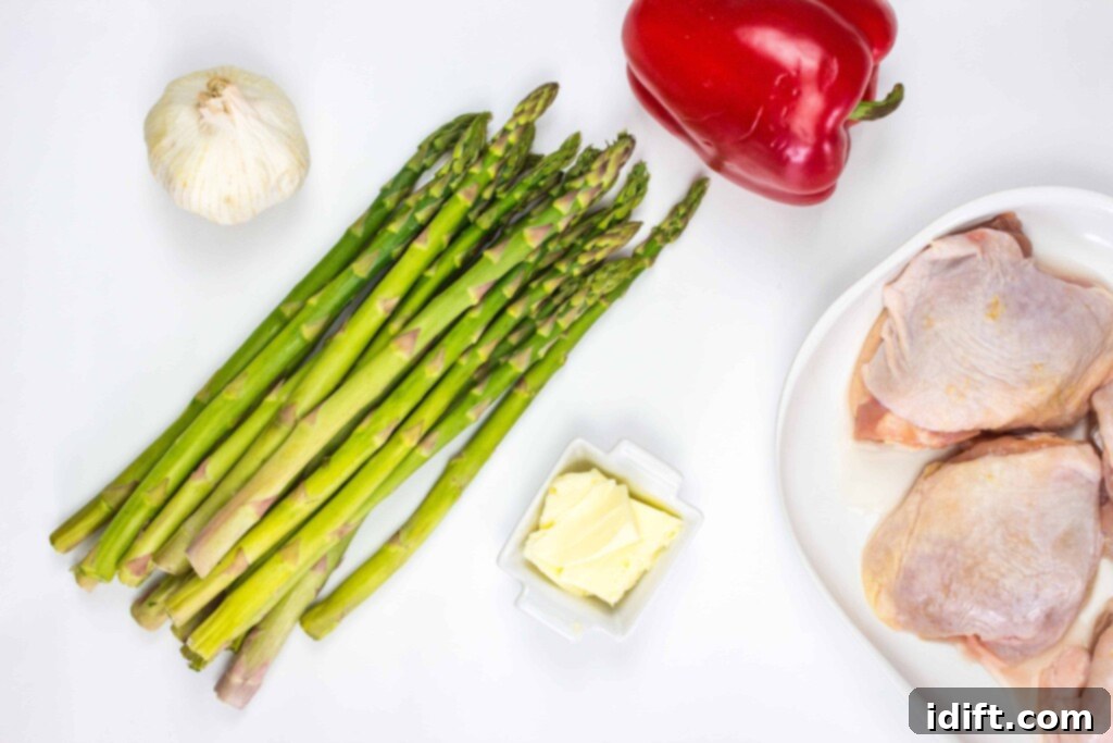 Roasted Garlic Chicken and Asparagus 4 A collection of fresh ingredients laid out on a cutting board, including chicken thighs, asparagus, red bell pepper, and garlic, ready for cooking.
