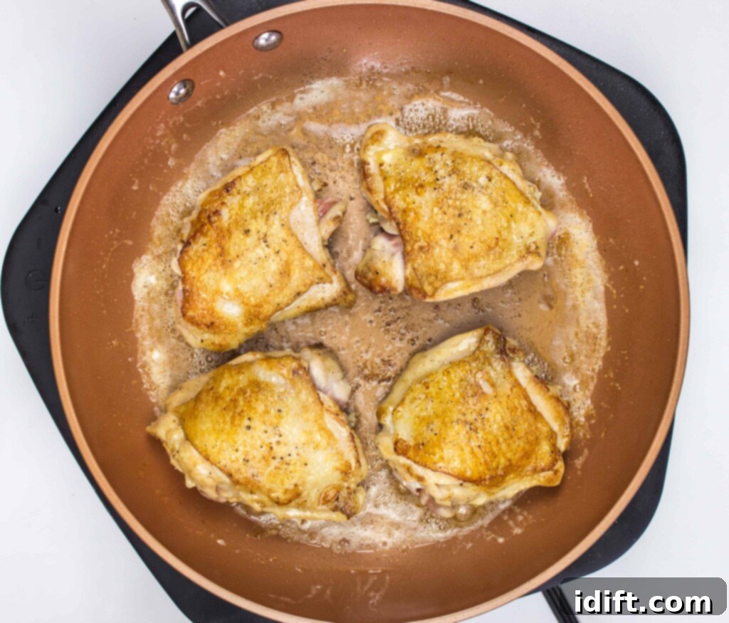 Roasted Garlic Chicken and Asparagus 7 Seared chicken thighs, now golden and crispy on both sides, resting in the skillet before other ingredients are added.
