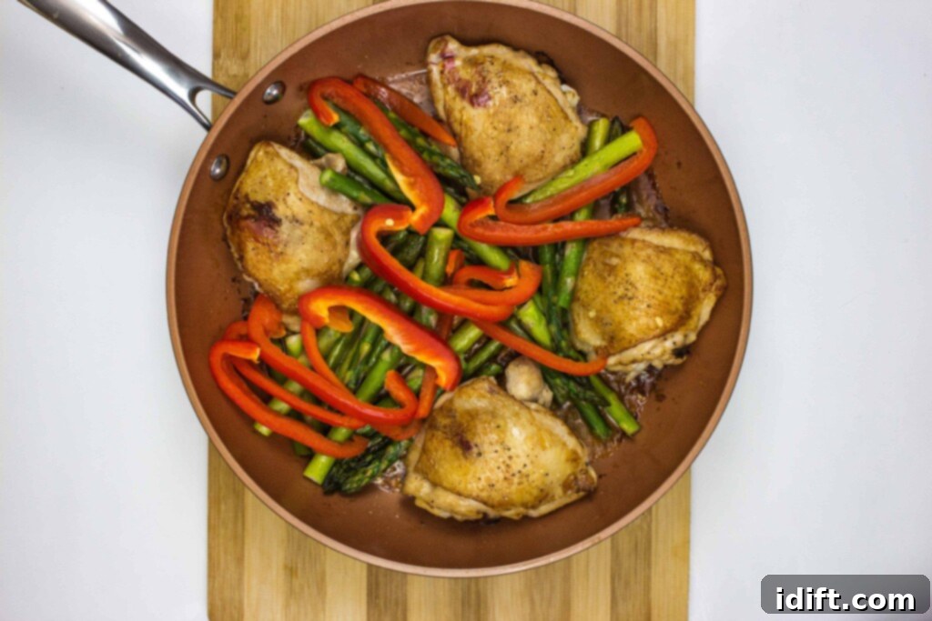 Roasted Garlic Chicken and Asparagus 8 Asparagus spears and sliced red bell pepper arranged around the browned chicken thighs in the skillet, ready for the oven.