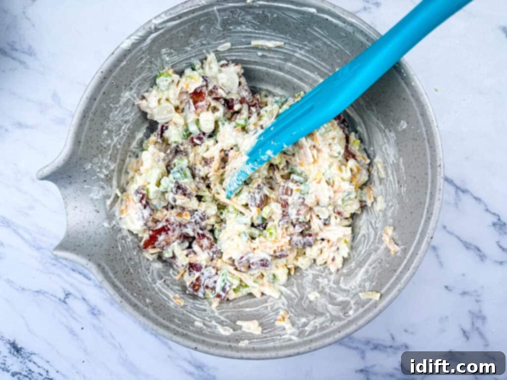 Diced potatoes, shredded cheddar cheese, and green onions being combined in a large bowl with the creamy sauce.