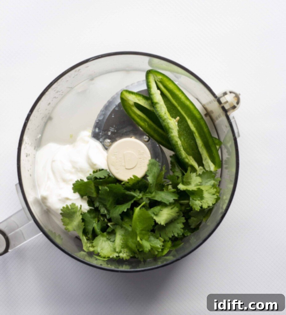 Zesty Jalapeño Cloud 5 All the fresh ingredients for creamy jalapeno dip, including sour cream, cilantro, jalapeno, lime, and ranch dressing powder, are shown loaded into a food processor, ready for blending.