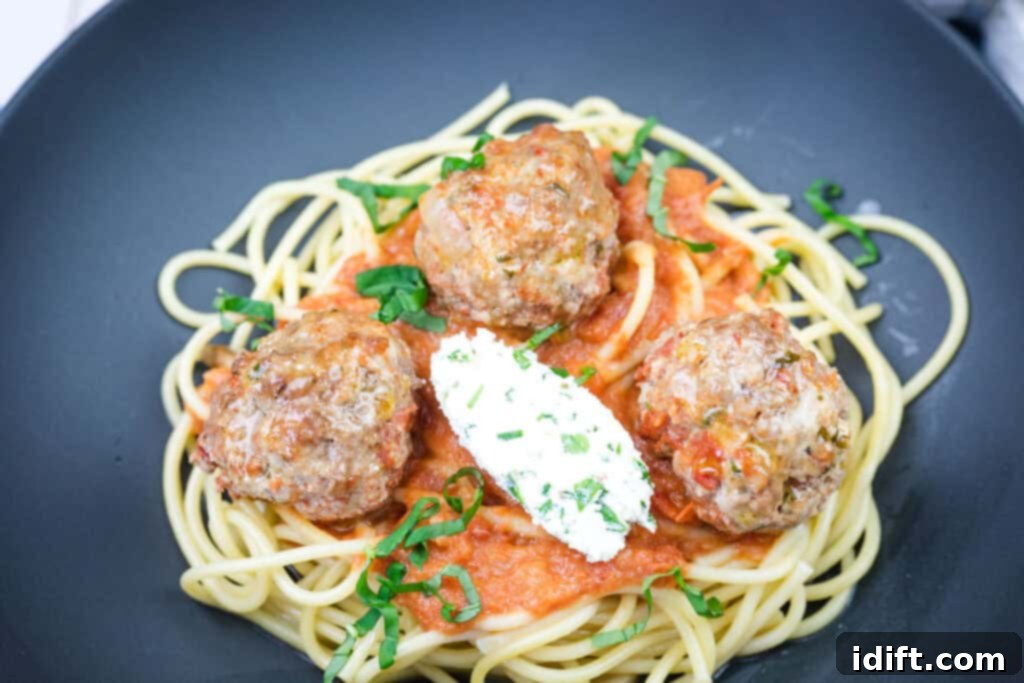 Cloud-Like Ricotta Meatballs with Rich Tomato Sauce 14 A delicious serving of spaghetti with ricotta meatballs and tomato sauce on a black plate, garnished with fresh basil leaves.