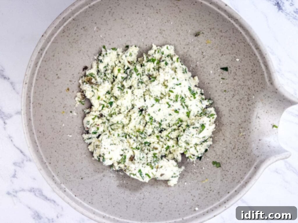 Cloud-Like Ricotta Meatballs with Rich Tomato Sauce 7 A bowl containing a mixed blend of ricotta, parmesan cheese, fresh parsley, chives, basil, lemon zest, capers, garlic powder, onion powder, and red pepper flakes on a white marble countertop.