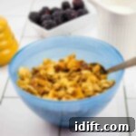 honey almond granola in a blue bowl with a spoon and berries in the background