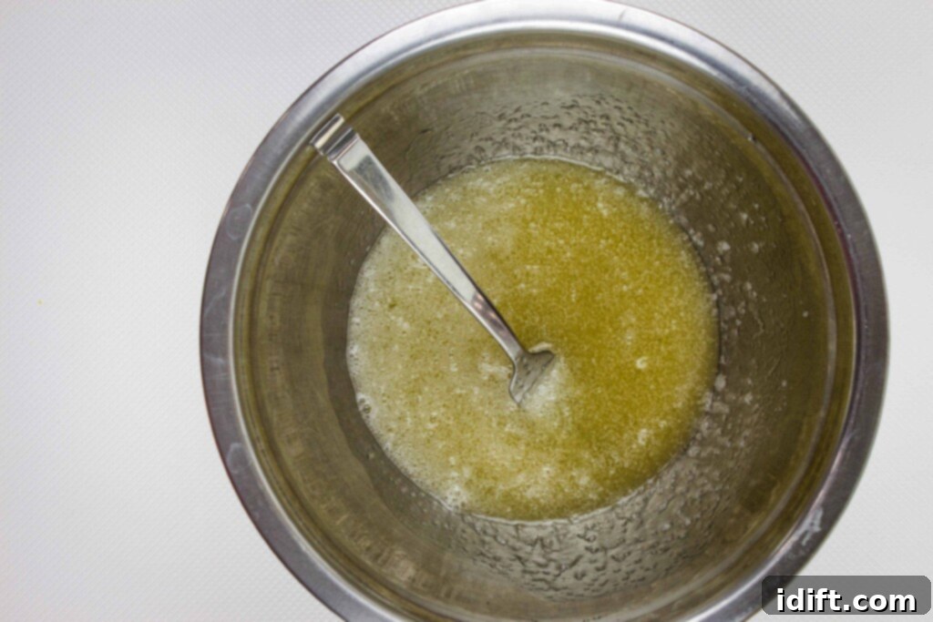 A glass bowl holds a rich, golden mixture of cooking oil and honey, expertly blended and ready for the next step in making honey almond granola.