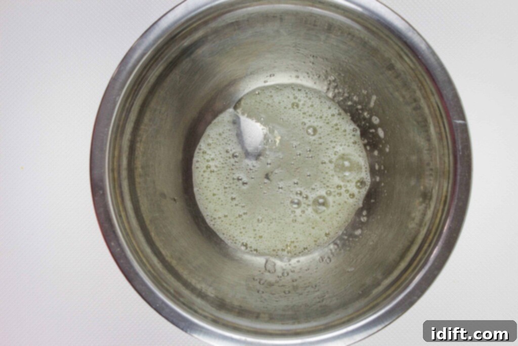A close-up shot of a frothy, whisked egg white in a clear glass bowl, ready to be incorporated into the granola mixture.
