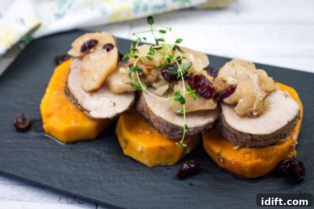 A serving of Slow Cooker Pork Tenderloin with Sweet Potatoes & Apples on a sleek black platter, beautifully presented.