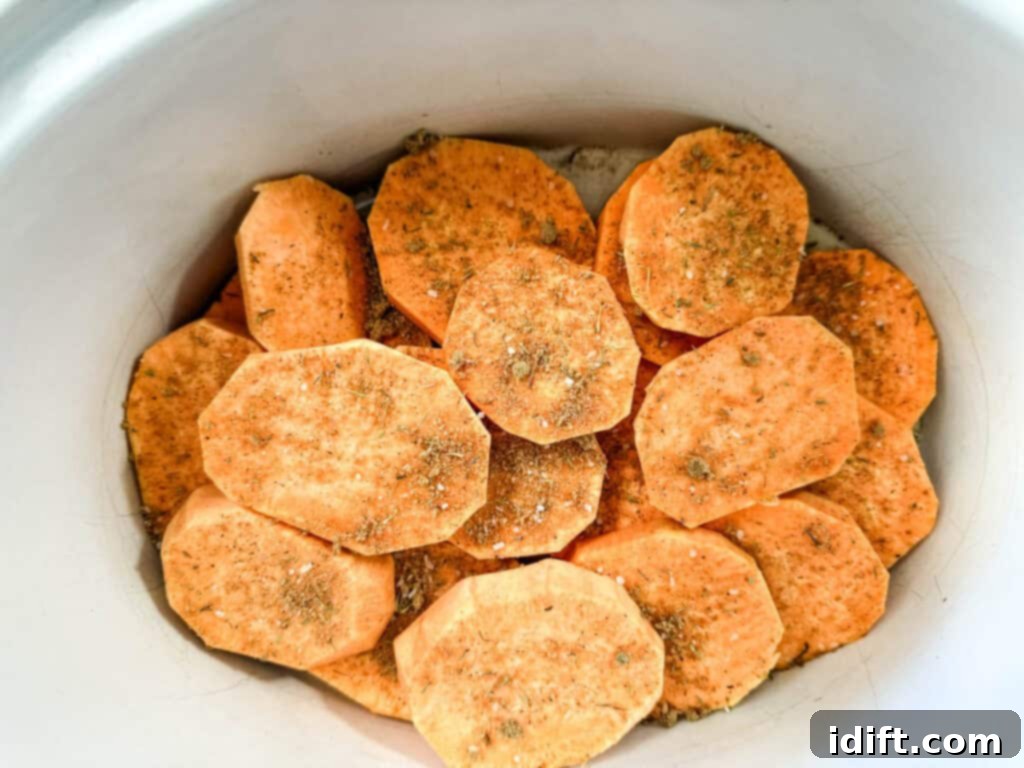 Sliced sweet potatoes arranged at the bottom of a slow cooker, ready for the next layer of ingredients.
